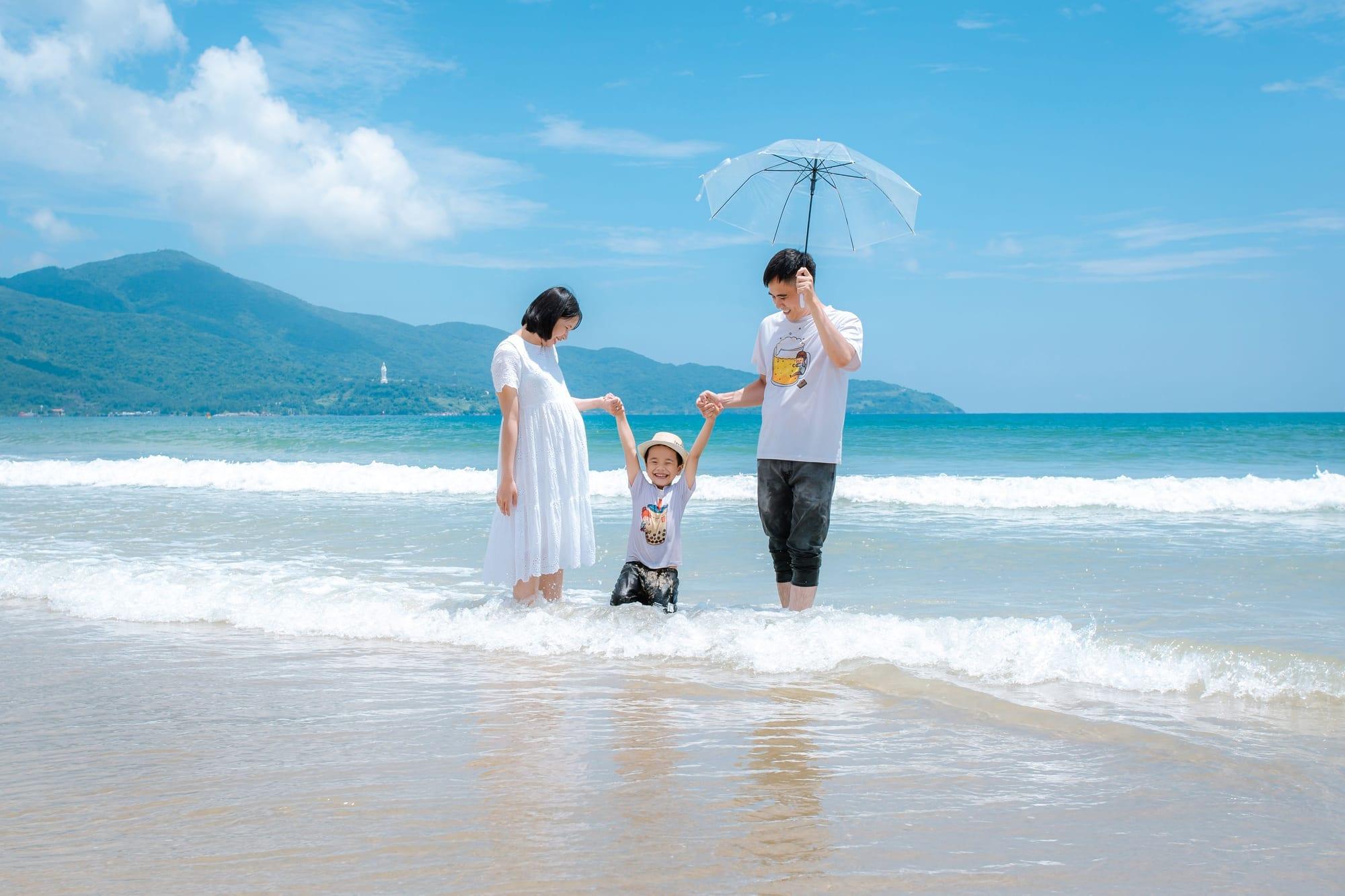 A young family walking together along the beach, sheltered under an umbrella